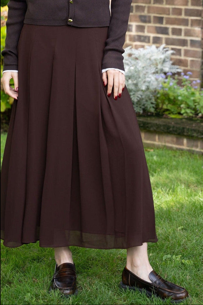 Woman in a brown outfit standing in a garden with a brick building in the background